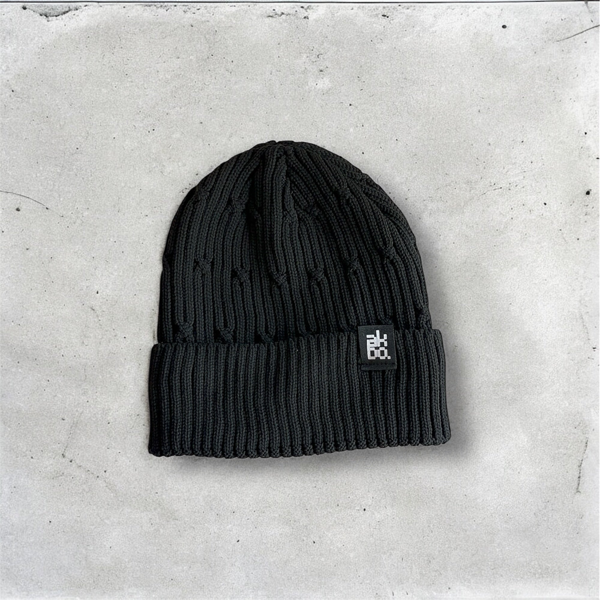 Black beanie with a logo on a gray concrete surface